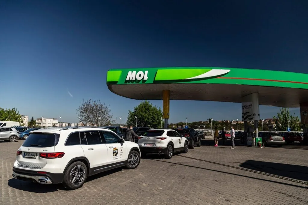 Stație de alimentare MOL cu mașini parcate și cer senin.
