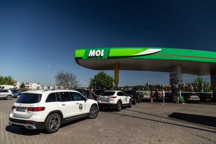 Stație de alimentare MOL cu mașini parcate și cer senin.