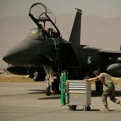 Un pilot pregătește un F-15E pe o pistă de decolare, în fundal munți arizi.