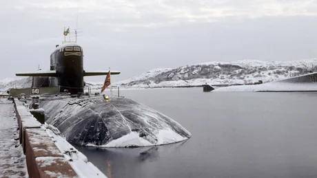 Submarin în apă rece, pe fundalul peisajului arctic acoperit cu zăpadă.