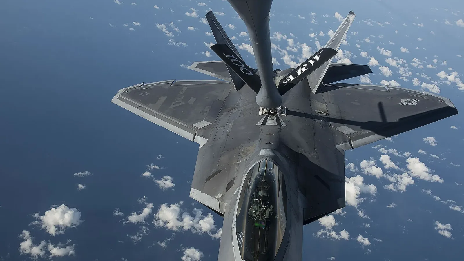 Avion militar realimentându-se în aer, cu nori pe fundal.