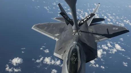 Avion militar realimentându-se în aer, cu nori pe fundal.