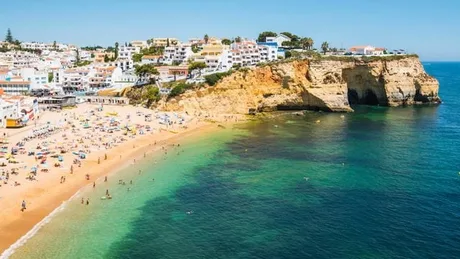 Plajă frumoasă în Algarve, cu ape cristaline și case colorate pe mal.