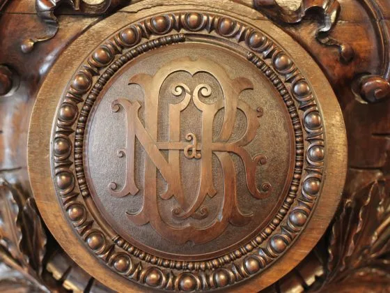 Sigla BNR gravată pe un fundal din lemn sculptat.