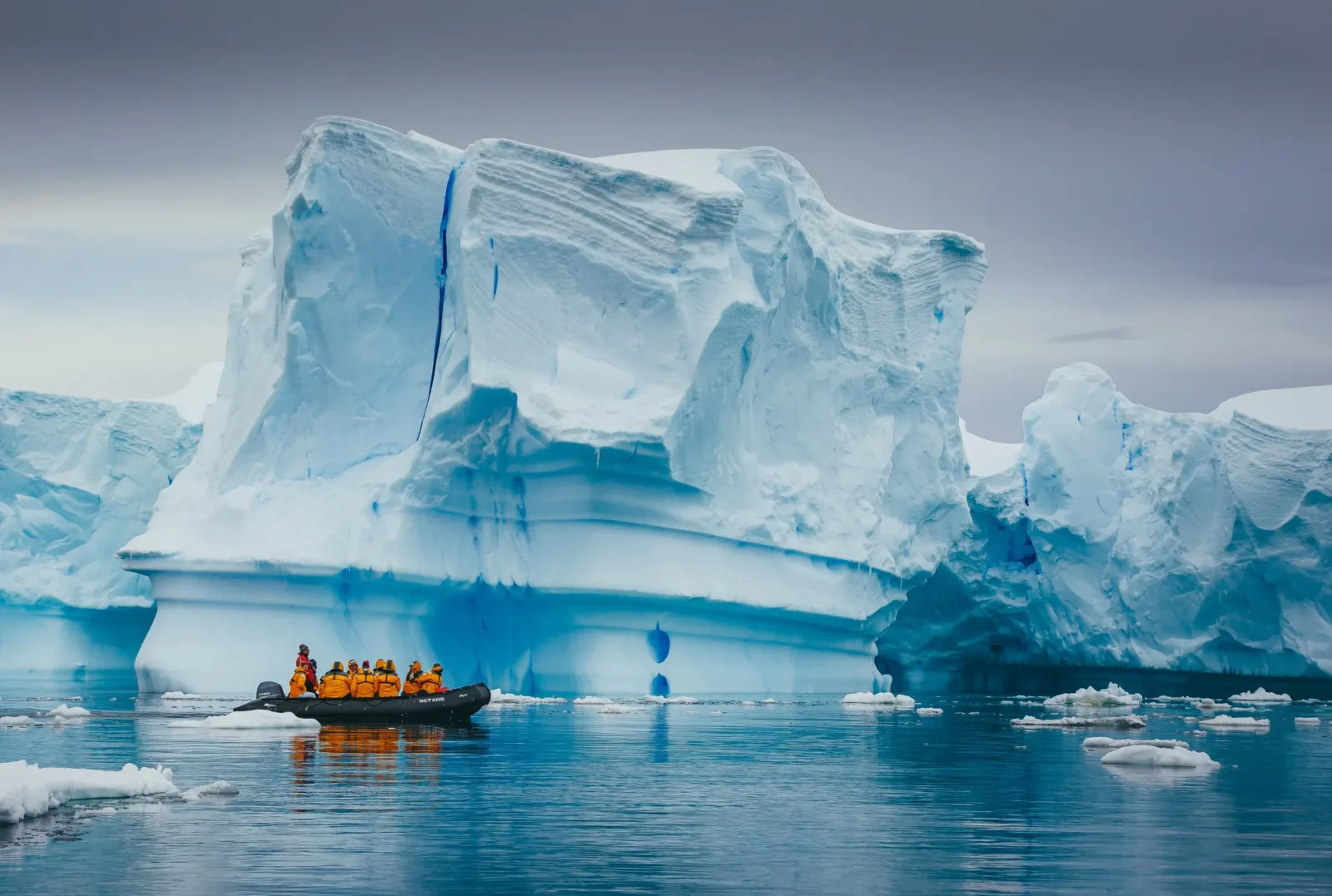 O echipă pe o barcă lângă un iceberg imens în Antarctica.