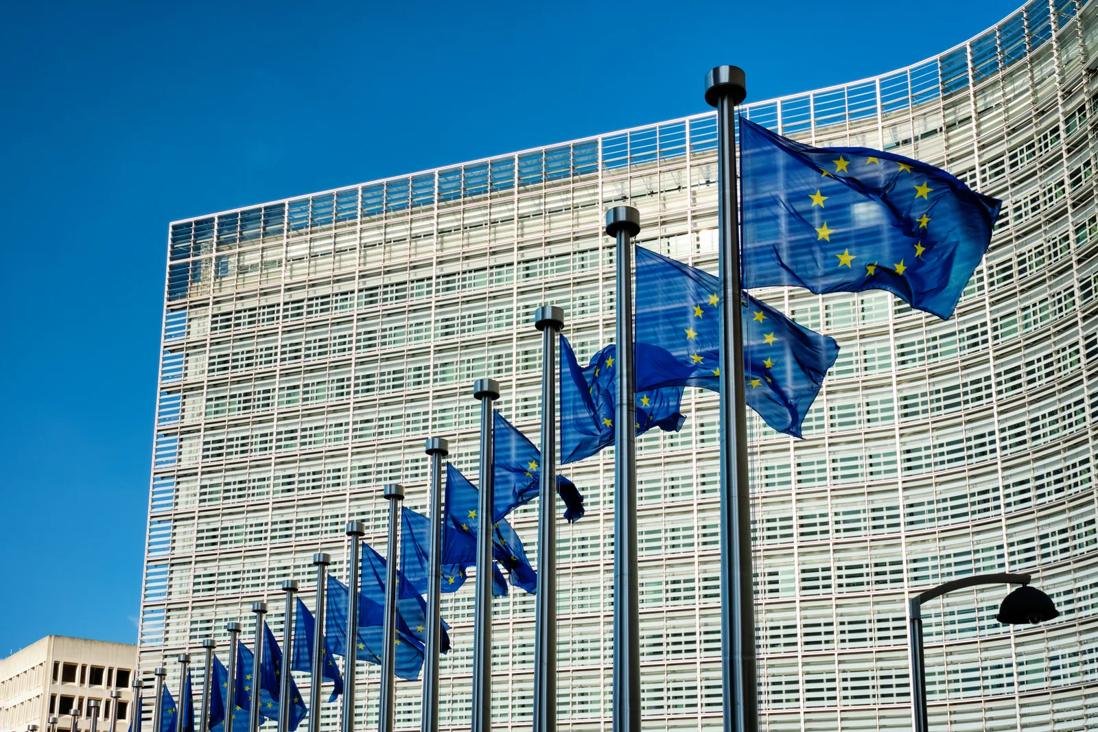 Clădirea Comisiei Europene cu steaguri ale Uniunii Europene fluturând în vânt.