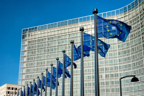 Clădirea Comisiei Europene cu steaguri ale Uniunii Europene fluturând în vânt.