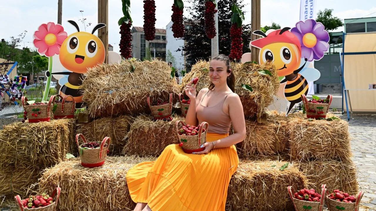 Femeie zâmbitoare pe fundal cu stupi și fructe de sezon la festival.