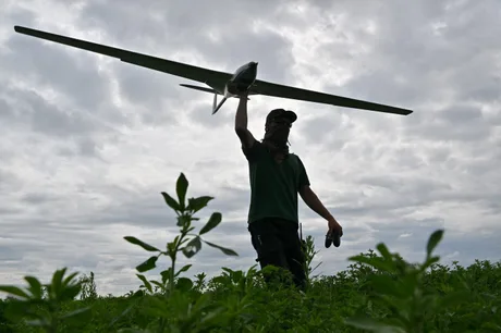 Un bărbat lansează o dronă pe un câmp verde sub un cer înnorat.