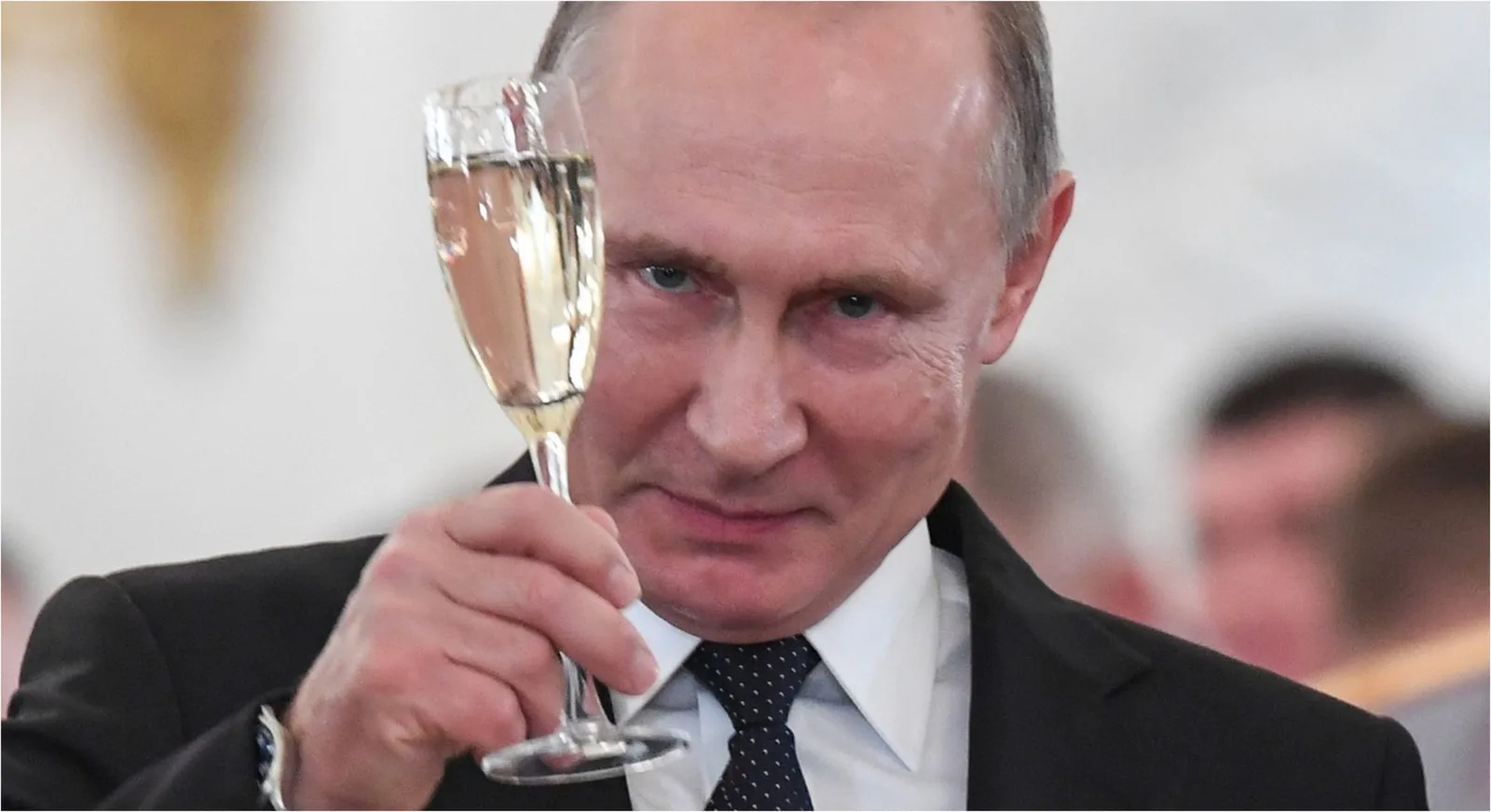 Vladimir Putin ținând un pahar cu băutură în mână, zâmbind.