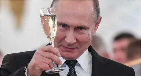 Vladimir Putin ținând un pahar cu băutură în mână, zâmbind.
