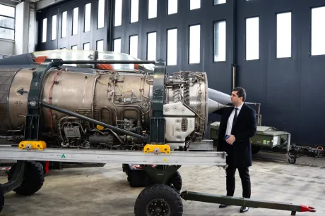 Un motor de avion militar inspectat de un bărbat îmbrăcat elegant.
