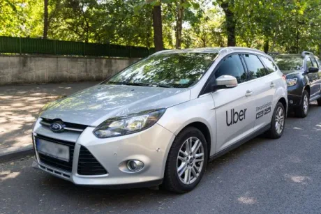 Mașină Uber parcată într-o zonă verde, sub copaci, într-o zi însorită.