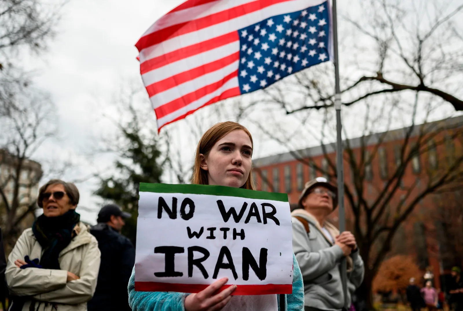 Protest împotriva războiului cu Iranul, cu steagul american în fundal.