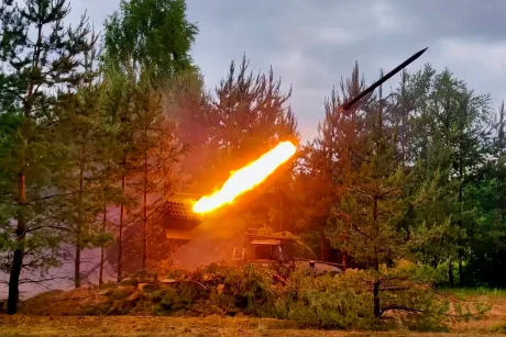 Rachete lansate în timpul unui atac militar, cu flacără intensă și vegetație în fundal.