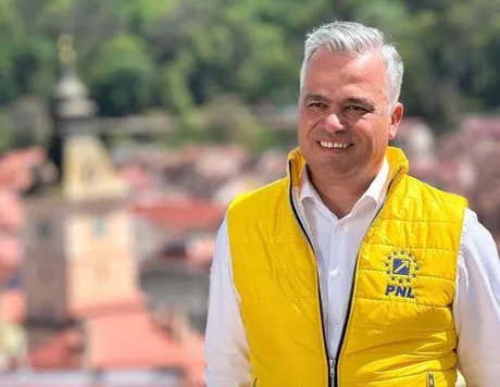 Reprezentant al Guvernului Veștea zâmbind, cu un peisaj urban în fundal.