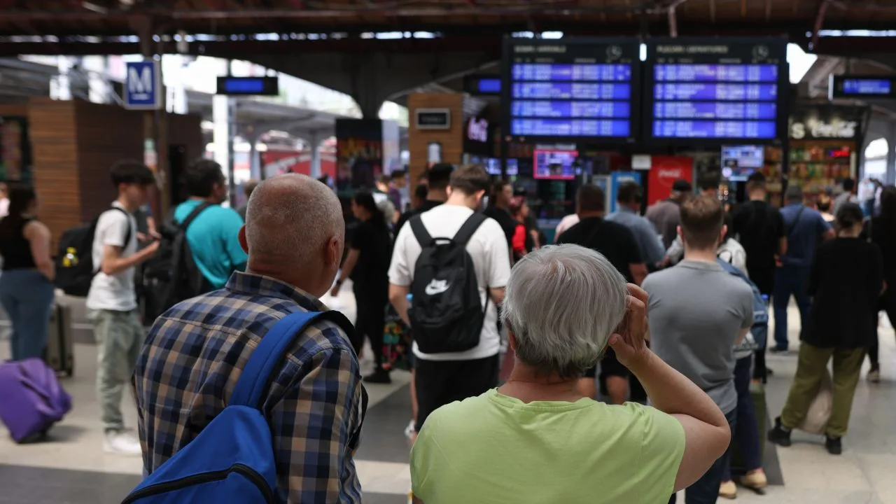 Oameni așteptând în Gara de Nord din București, cu panouri de informații în fundal.