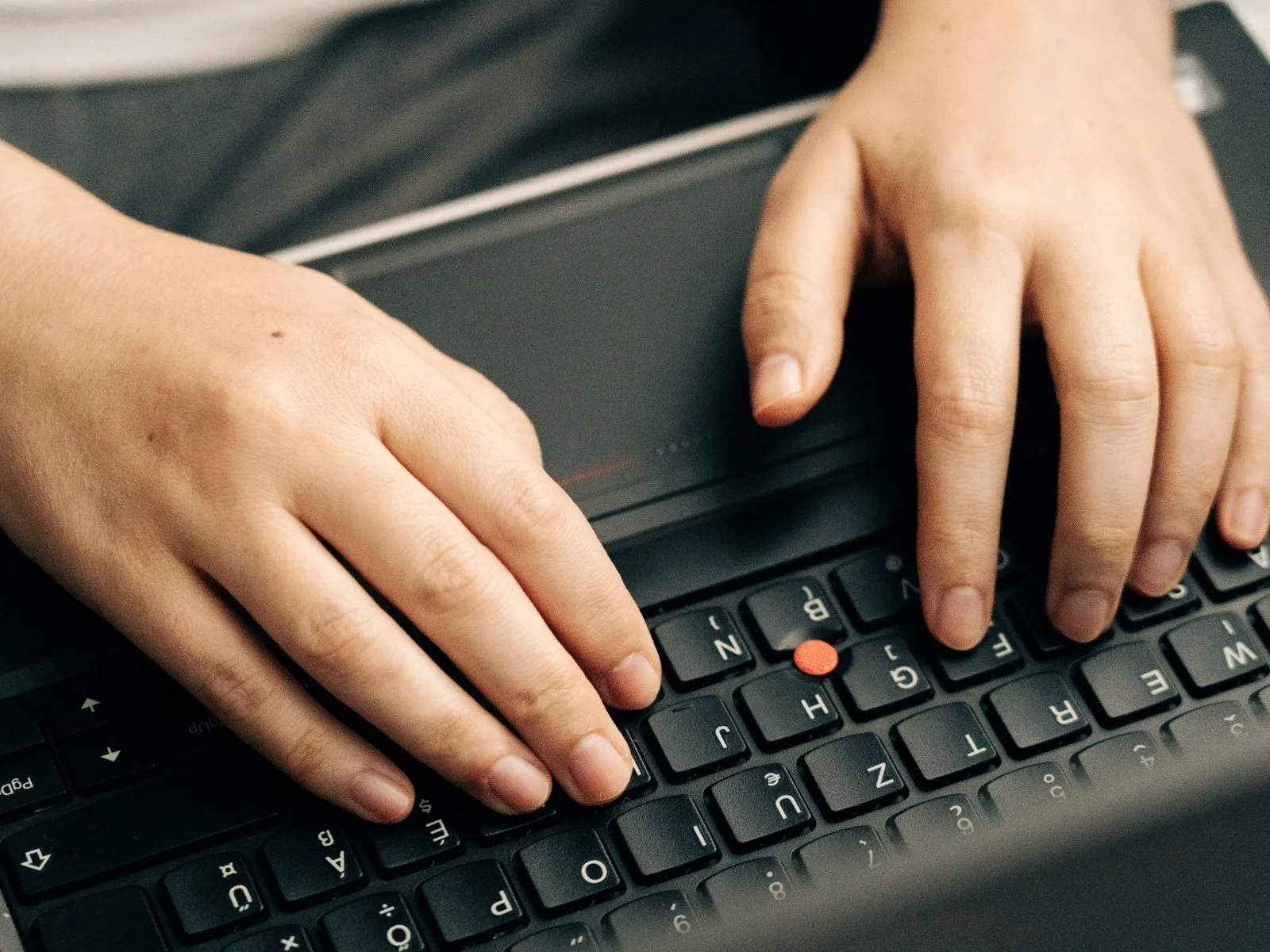Mâini care tastează pe un laptop, evidențiind activitatea de programare.