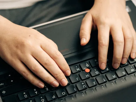 Mâini care tastează pe un laptop, evidențiind activitatea de programare.