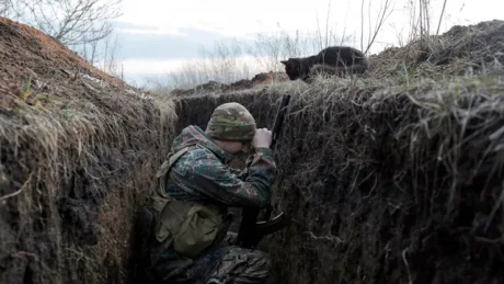 Soldat ucrainean în tranșee, observând atent împrejurimile în timpul conflictului.