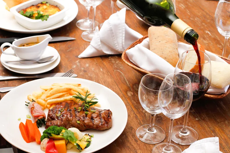 Mâncare gourmet servită pe o masă elegantă, cu vin și accesorii de restaurant.