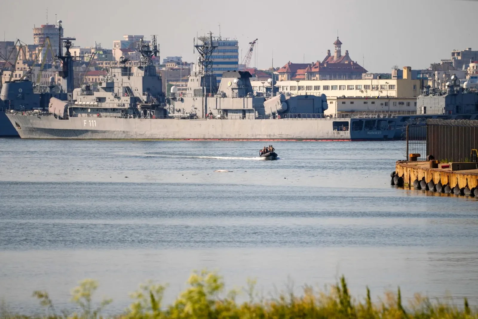 Vapor pe apă în apropierea portului Constanța, cu nave militare în fundal.
