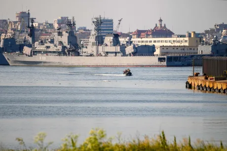 Vapor pe apă în apropierea portului Constanța, cu nave militare în fundal.