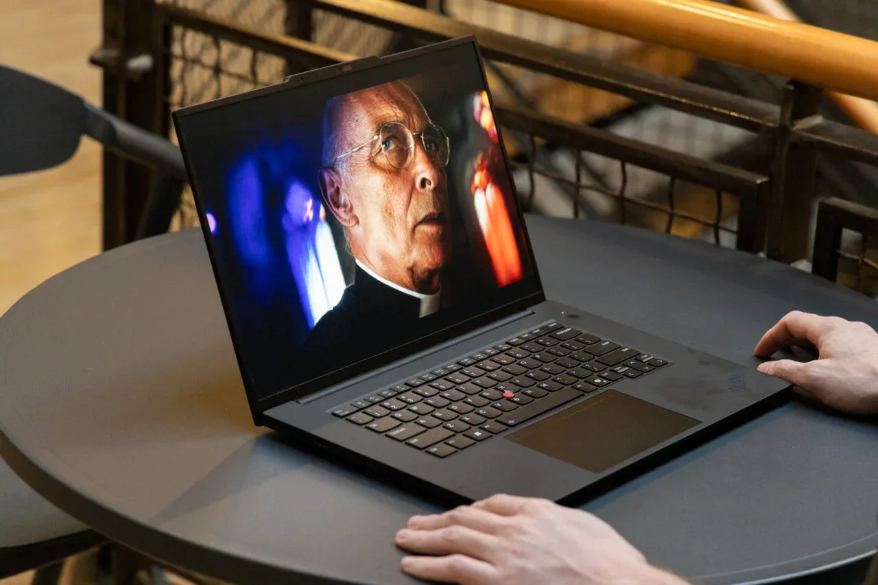 Laptop deschis pe o masă, cu un bărbat care îl folosește, afișând un film.