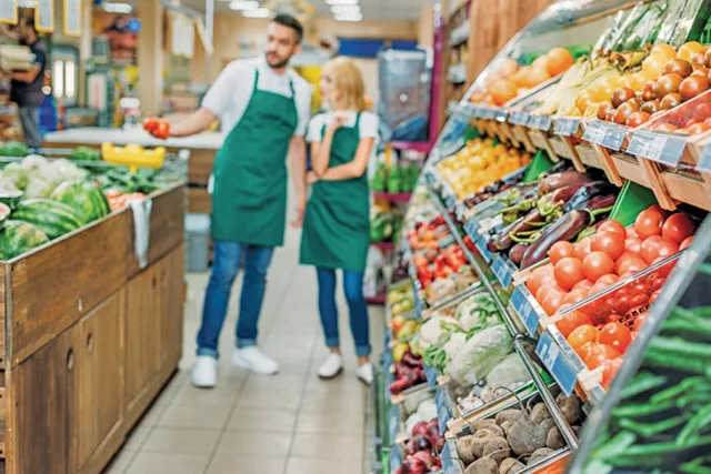 Retaileri în supermarket, expunere de legume și fructe proaspete.