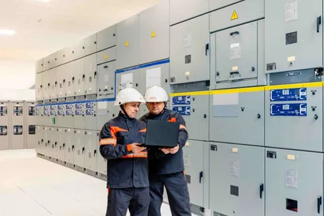Specialiști analizând echipamente electrice într-o stație de transformare.