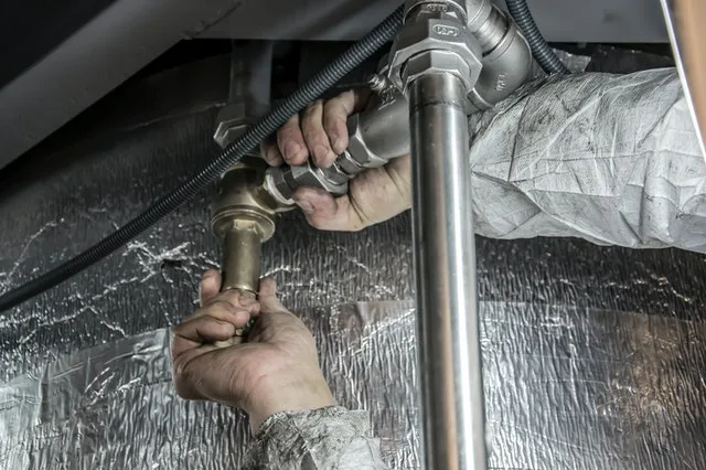 Mâini lucrând la un sistem de țevi, simbolizând meserii tradiționale.
