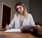 Femeie scriind la birou, documente pe masă.