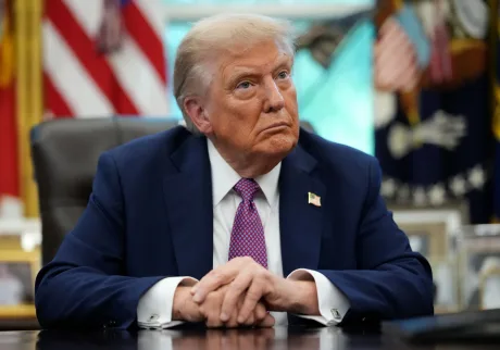 Donald Trump ascultând în biroul Oval, cu steaguri în fundal.