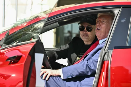 Elon Musk și Donald Trump într-un automobil Tesla roșu, discutând despre viitorul industriei auto.