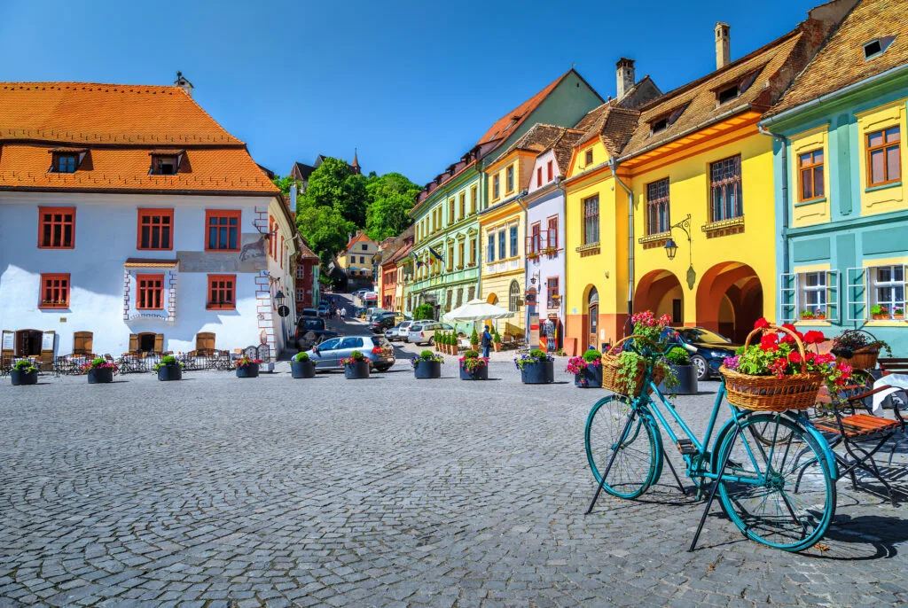 Străduțe pitorești dintr-un oraș românesc, cu clădiri colorate și o bicicletă decorată.