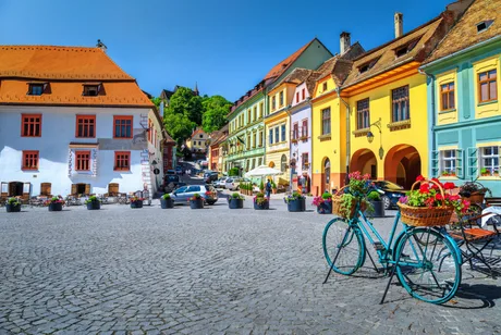 Străduțe pitorești dintr-un oraș românesc, cu clădiri colorate și o bicicletă decorată.