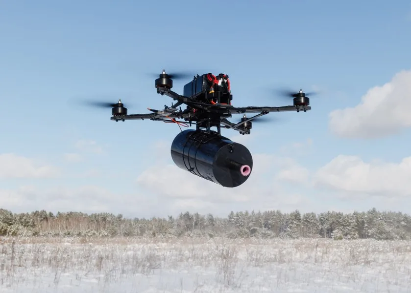 Dronă echipată cu un dispozitiv de atac, zburând pe un fundal de pădure.