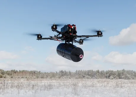 Dronă echipată cu un dispozitiv de atac, zburând pe un fundal de pădure.