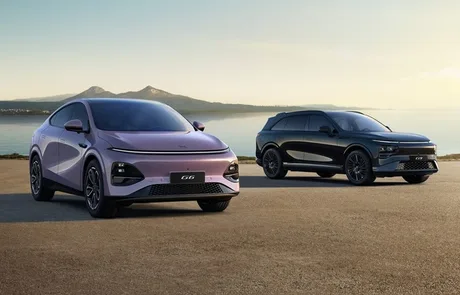 Două modele electrice BYD parcate pe malul mării, cu peisaj montan în fundal.