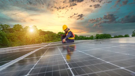 Instalare panouri solare pe acoperiș, cu soarele apunând în fundal.