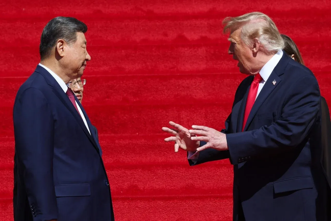 Donald Trump și Xi Jinping discutând pe treptele unei clădiri, cu un fundal roșu.
