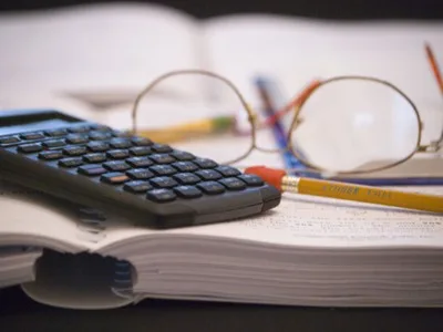 Calculator și ochelari pe un birou plin de documente.
