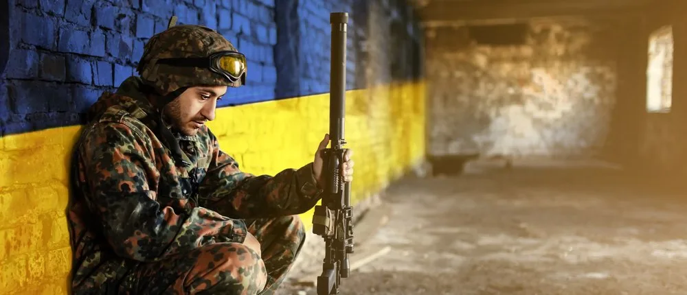 Soldat ucrainean meditând în fața unui zid colorat în galben și albastru.