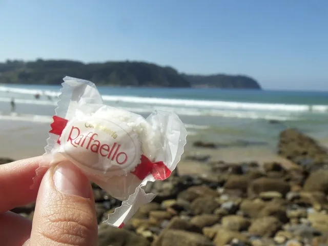 Un Raffaello ținut în mână pe plajă, cu marea în fundal.