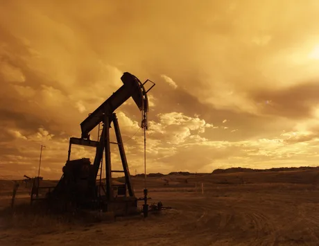 O pompă de petrol într-un peisaj arid, sub un cer portocalie.