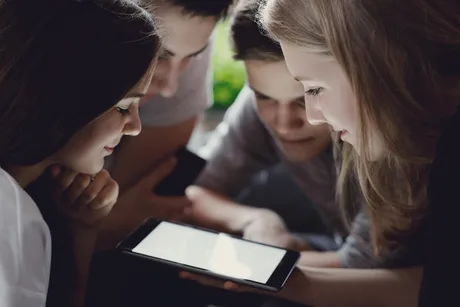 Adolescenți români discutând și interacționând în jurul unui dispozitiv mobil.