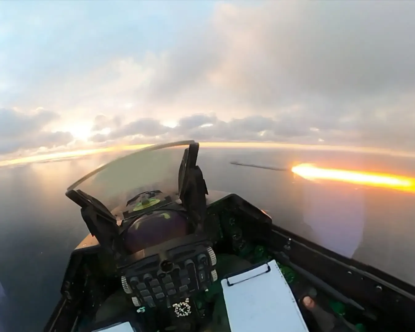 Pilot în cockpitul unui avion militar, observând un zbor deasupra mării.