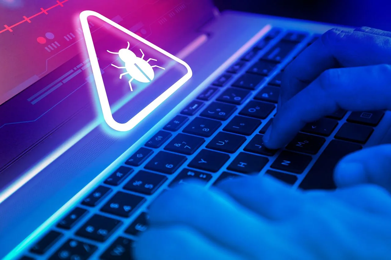 O mână tastează pe un laptop cu un simbol de alertă pe ecran.