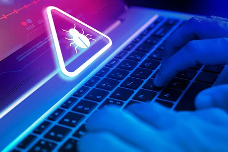 O mână tastează pe un laptop cu un simbol de alertă pe ecran.