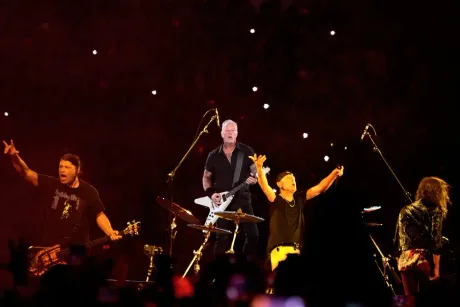Metallica cântă pe scenă, public entuziast în fundal.